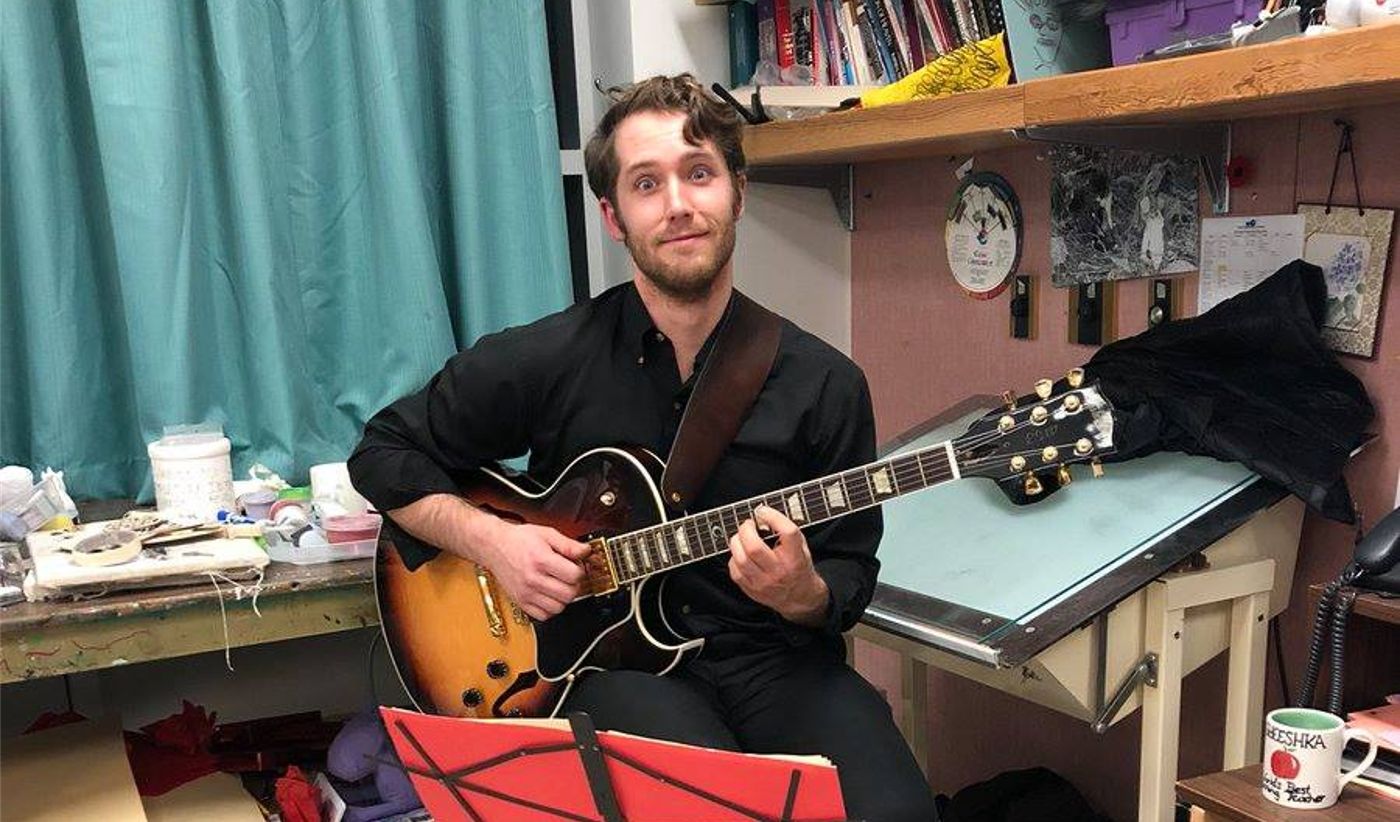 Jeremy sitting in classroom with a guitar smiling
